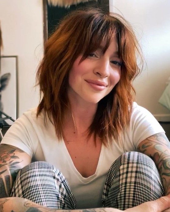 a shaggy medium-length copper haircut with messy waves and bottleneck bangs is a cool and bold idea