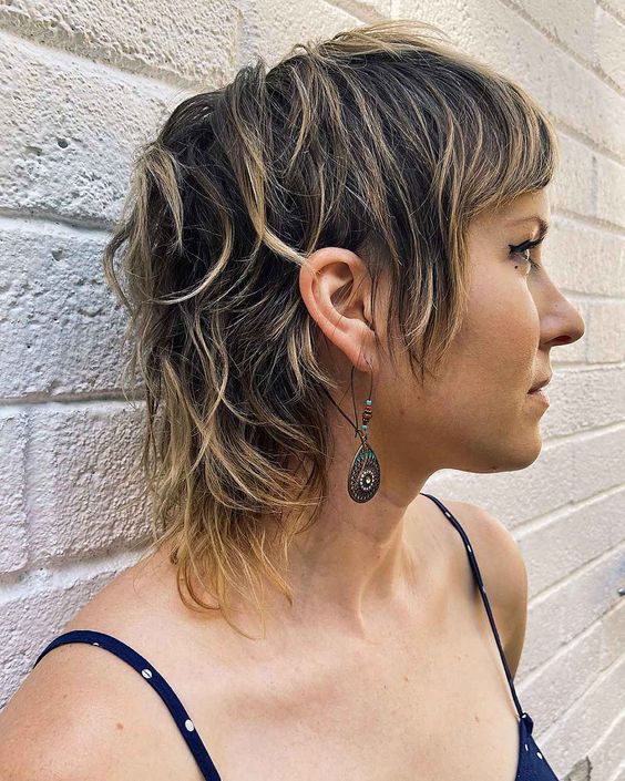 a short brunette mullet with blonde balayage and bangs plus a bit of messy texture looks all-natural