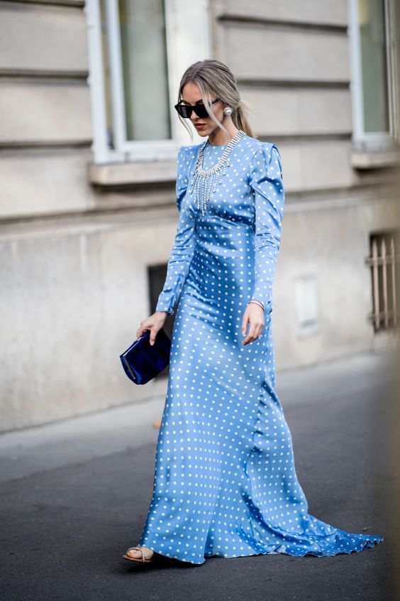 a blue maxi polka dot dress with draped sleeves, a train and a high neckline, a statement necklace and pearl earrings
