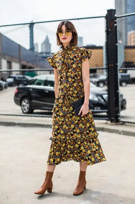 a bold and chic fall wedding guest look with a yellow, black and navy floral midi dress with a high neckline, ruffle cap sleeves, brown boots and a black clutch