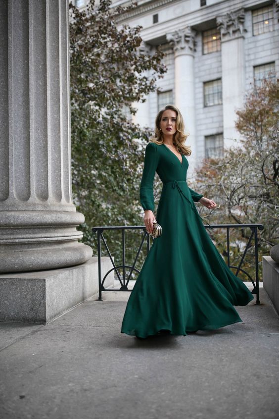 A bold green maxi dress with a deep V neckline, long sleeves, a small embellished clutch bag for a fall wedding