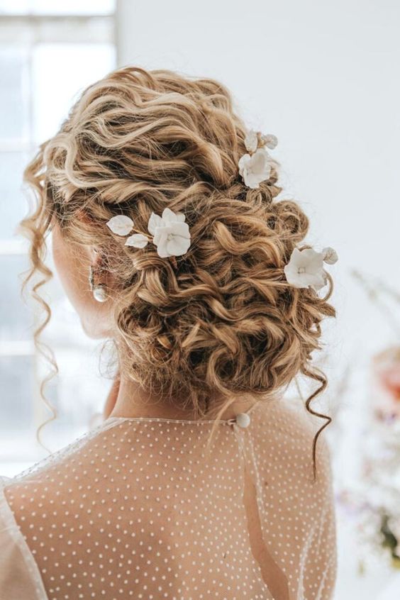 a curly low updo with curls down and some flowers tucked into hair is a lovely solution