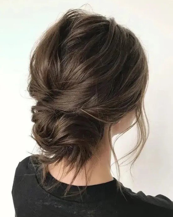 a messy and dimensional low bun with a messy bump on top and some locks down is a stylish and cool idea for a wedding