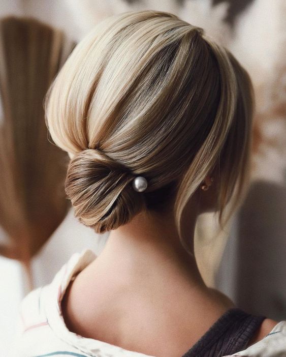 a modern and sleek low bun with a volume on top, face-framing hair and a pearl pin is a stylish and catchy idea
