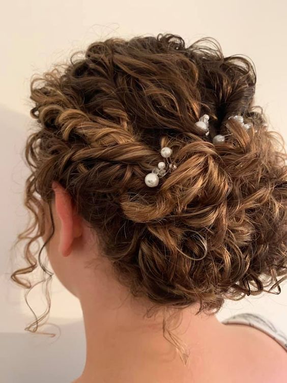 a curly wedding updo with tiwsts and curls on top and pearl hair pins for styling, curls down to frame the face