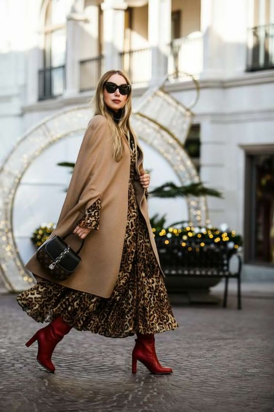 a leopard maxi dress with a high neckline, red boots, a tan capelet and a black midi bag for a bold fall wedding gues tlook