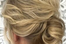 28 a low messy chignon with a wavy and messy top, on medium hair and with face-framing locks for a mother of the bride