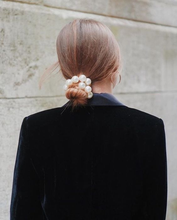 an elegant low bun with a sleek top and a pearl hair tie is a cool idea for a more formal wedding
