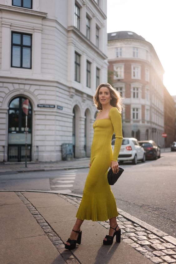 a neon yellow fitting midi dress with a square neckline, a pleated skirt, black platform shoes and a black clutch