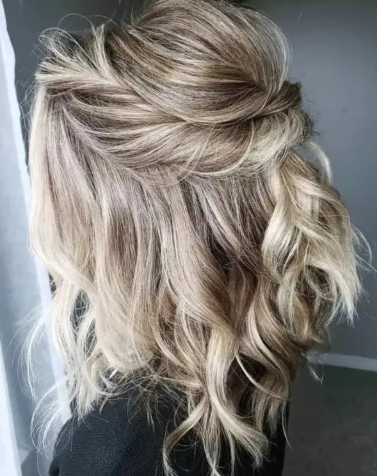 a beautiful blonde half updo with a bump on top and a twisted element and waves down is a stylish solution