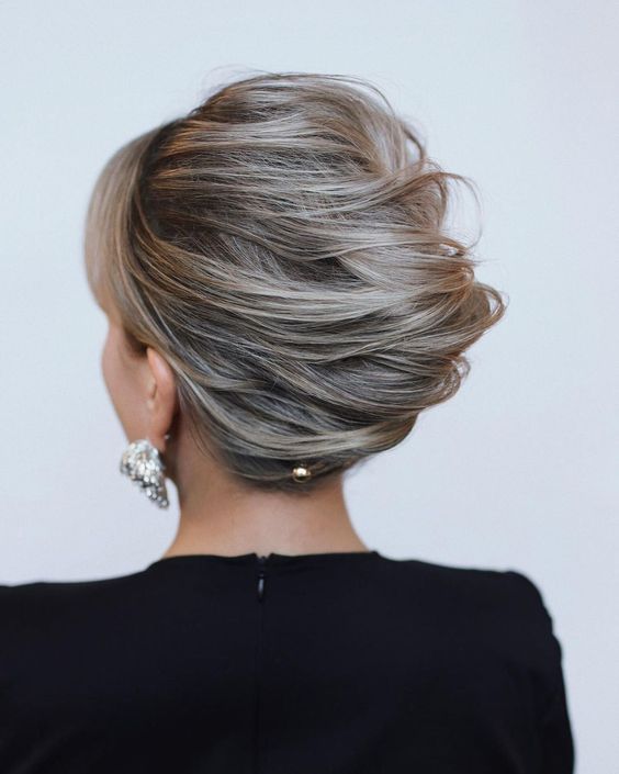 a messy and voluminous twisted chignon hairstyle with side bangs and a bit of hair pins is a stylish idea for a mother of the bride