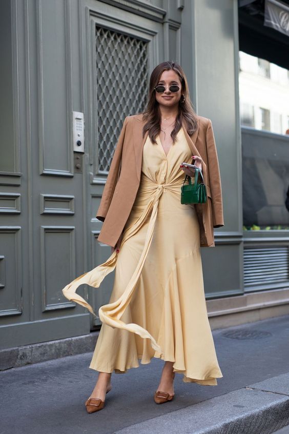 a pale yellow midi dress with a ruffle skirt, a brown blazer on top, brown buckle shoes and a small green bag