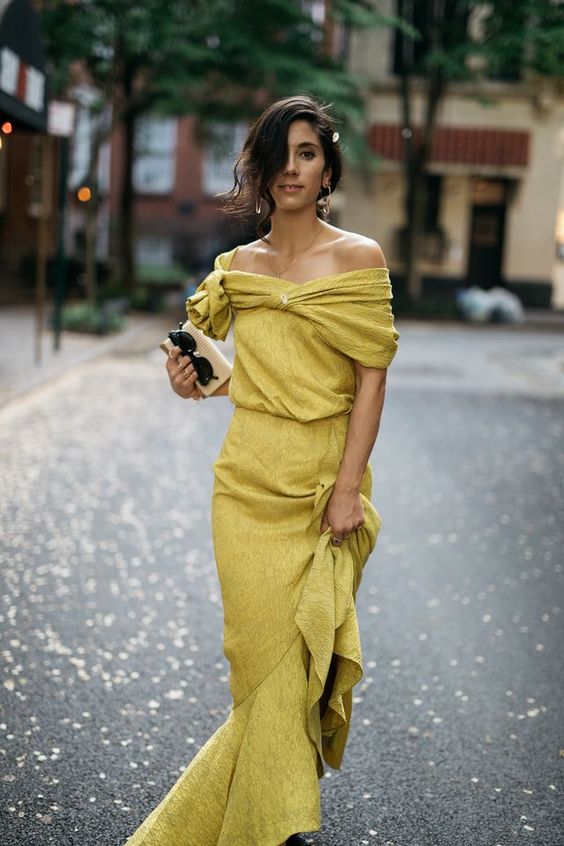a pale yellow off the shoulder maxi dress with a ruffle skit, a draped neckline, a mini bag and statement earrings for a fall wedding