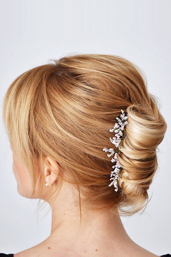 a twisted chignon with fresh blooms, a messy and voluminous bump on top, side bangs is a stylish idea for a mother of the bride