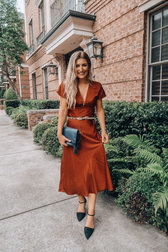 a rust-colored midi dress with a deep plunging neckline, short sleeves, a belt, black shoes and a black clutch