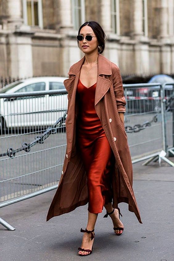 a rust-colored slip midi dress, a brown trench coat, brown bow shoes for a chic fall wedding guest look