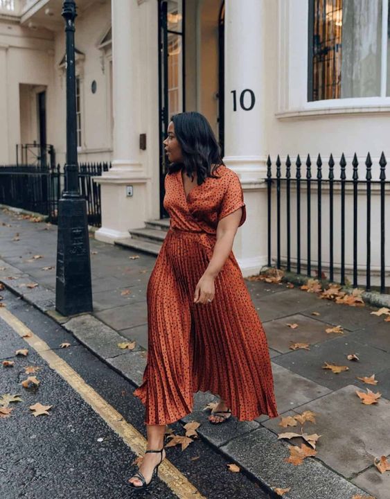 A spotted rust colored midi dress with a pleated skirt, black shoes are a cool combo for a fall wedding