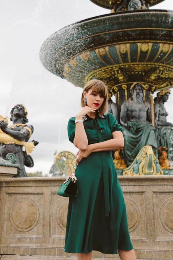An emerald midi A line dress with short sleeves, an embellished collar, a small grene bag and statement earrings