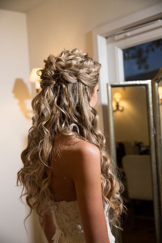 a curly half updo with a braid and curls down is a cool idea for a relaxed and chic bride with curly hair