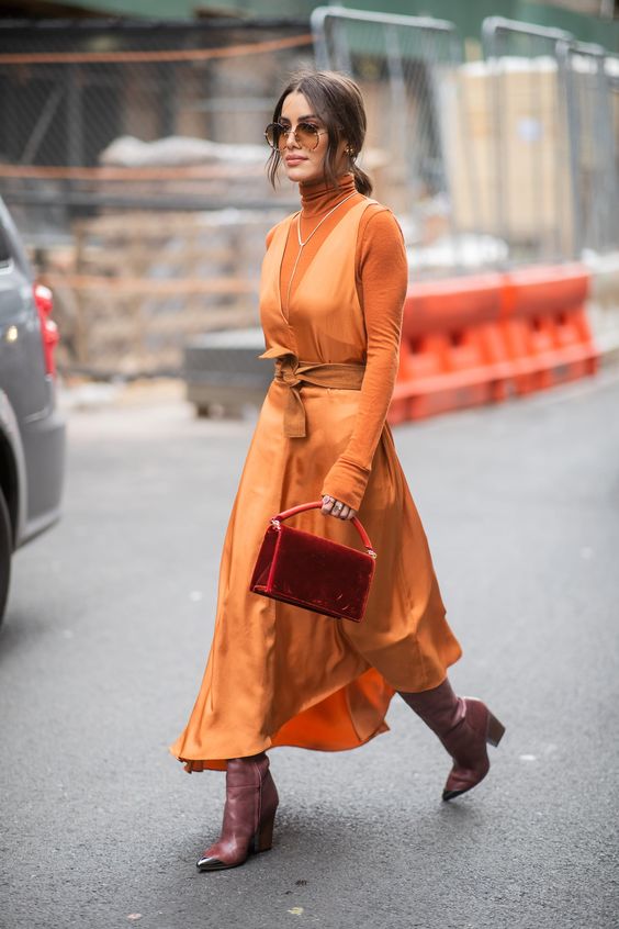 an orange turtleneck, an orange silk midi dress, mauve boots and a red velvet bag plus a necklace