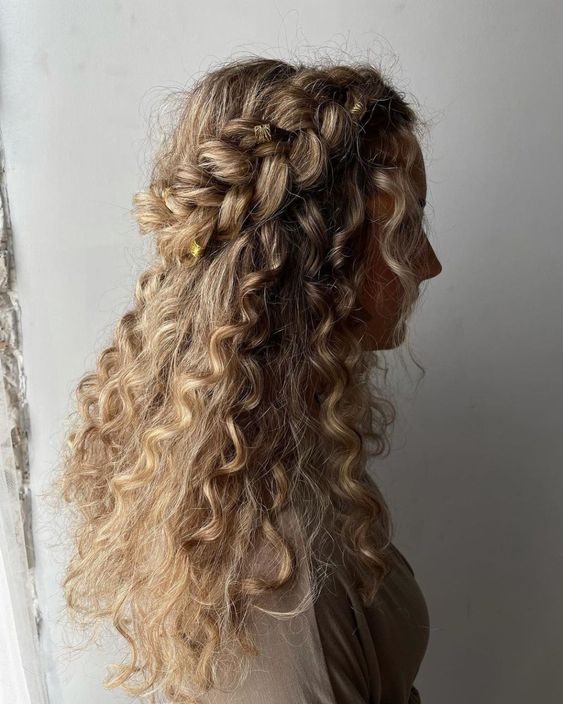 a curly half updo with a braided halo and curls down is a cool idea for a boho wedding