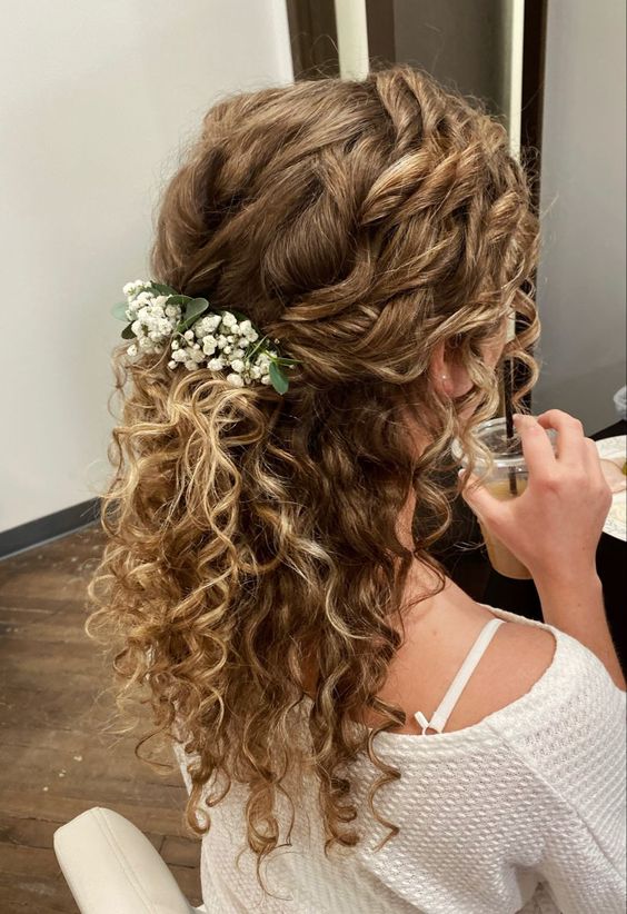 a naturally curly wedding half updo with a curly top and curls down plus white blooms and greenery tucked in