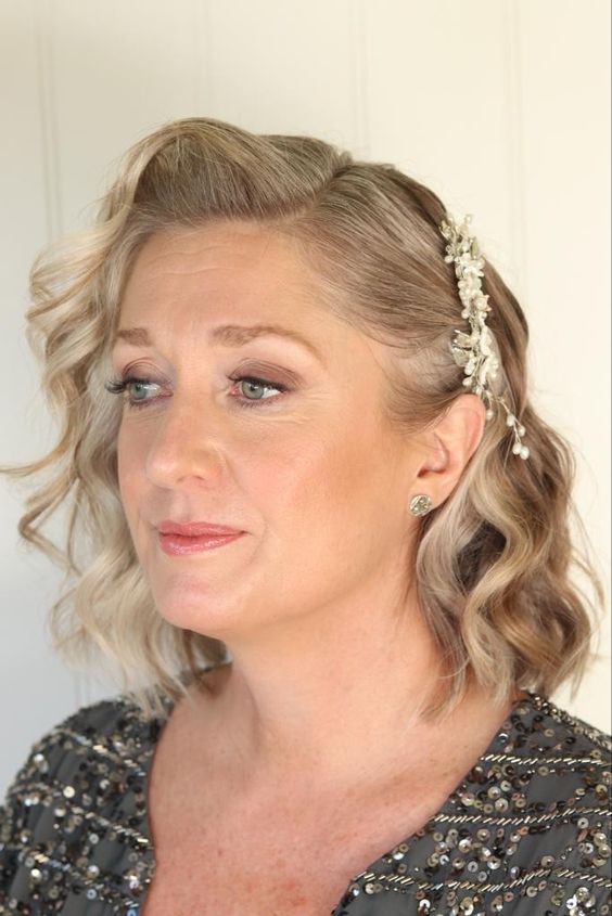 an elegant mother of the bride hairstyle with a floral harpiece fixing hair on one side, with waves is very stylish