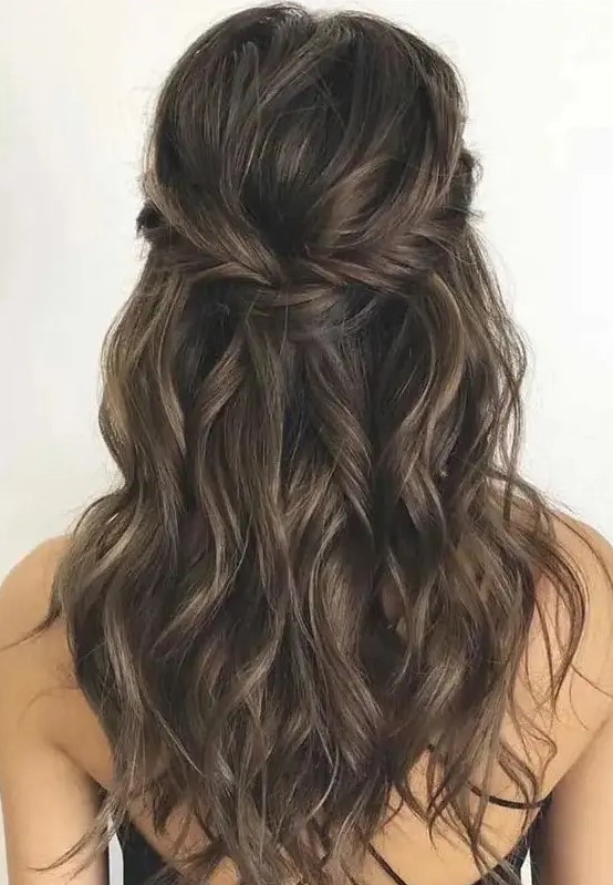a long half updo with a braided halo and waves down is a chic and cool idea for a boho wedding