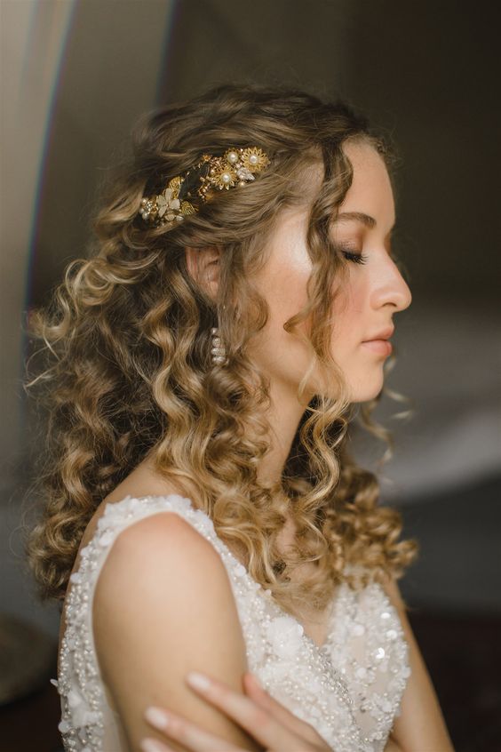 a sophisticated curly wedding half updo with twists, curls framing the face and a gold and pearl hairpiece on one side