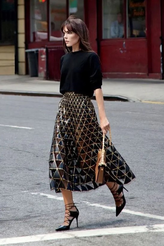 a black oversized sweater, a black and gold geometric midi skirt, black lace up shoes and a camel bag