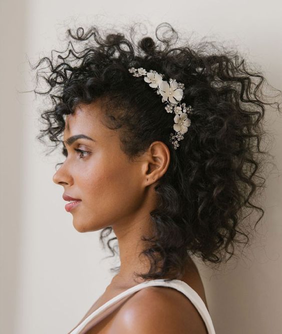 a curly hairstyle with a floral accent on one side and some curls down is a cool idea for a wedding