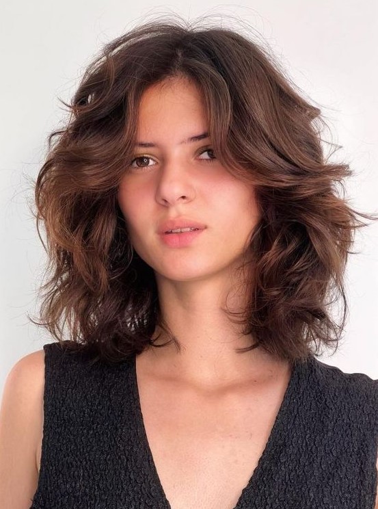 a beautiful dark brunette medium-length butterfly haircut on wavy hair, with a lot of dimension
