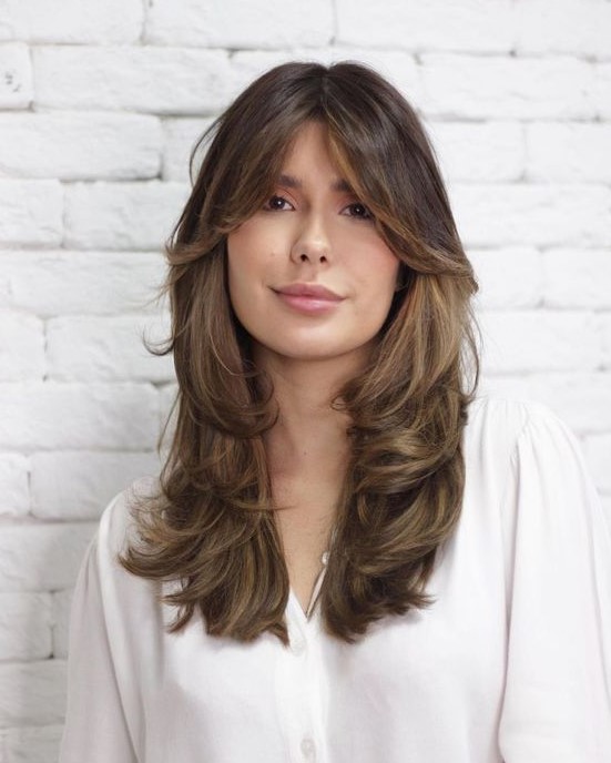 a beautiful long brown butterfly haircut with bottleneck bangs and caramel balayage plus curled ends is adorable