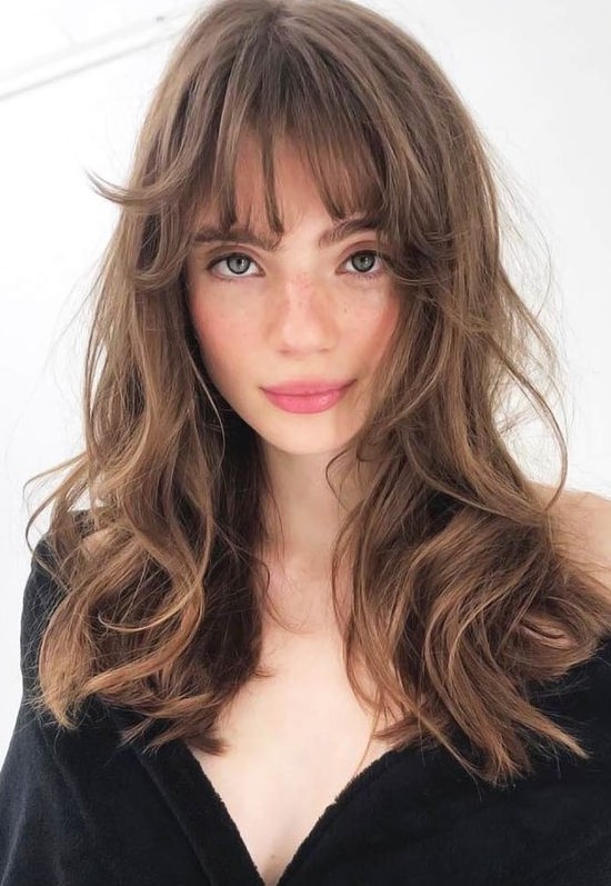 a beautiful long brunette butterfly haircut with messy waves and wispy bangs is a cool and relaxed idea to rock right now