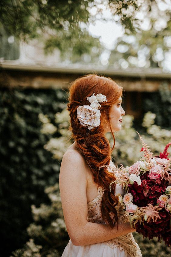 a beautiful messy side braid with a volume on top and some fabric flowers is a chic idea for a more relaxed bridal look
