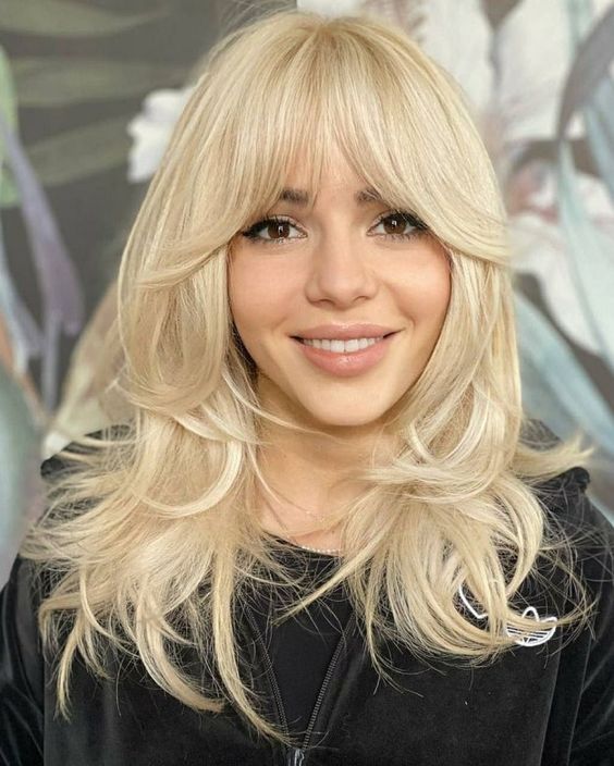 A bleached butterfly haircut on medium length hair, with some messy volume and bottleneck bangs is lovely