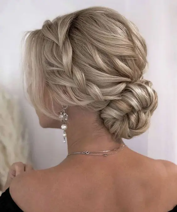 a blonde low bun with a braided halo and a braided top, face framing locks is a chic and stylish idea