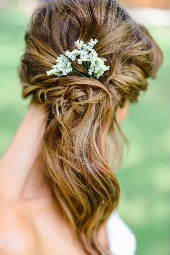 A boho side swept wavy hairstyle with a bump, a woven element and some fresh flowers tucked in
