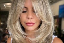 a chic blonde butterfly haircut of medium length, with curtain bangs and wavy ends is a cool and pretty solution