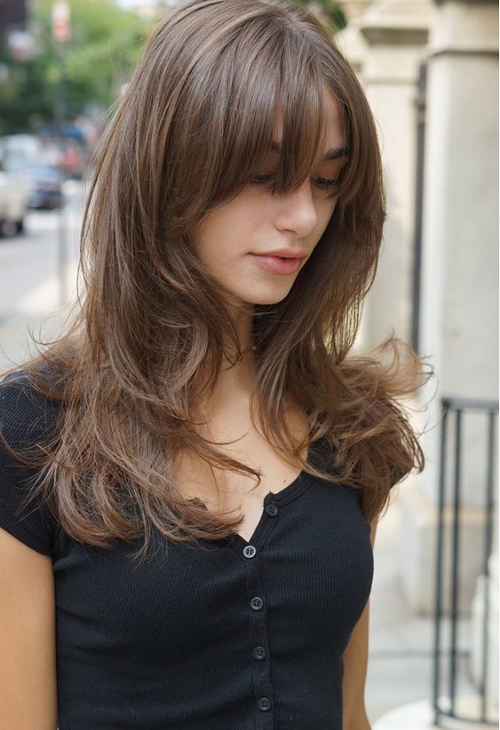 a chic light brunette long butterfly haircut with wispy bangs and waves is a cute and cool idea