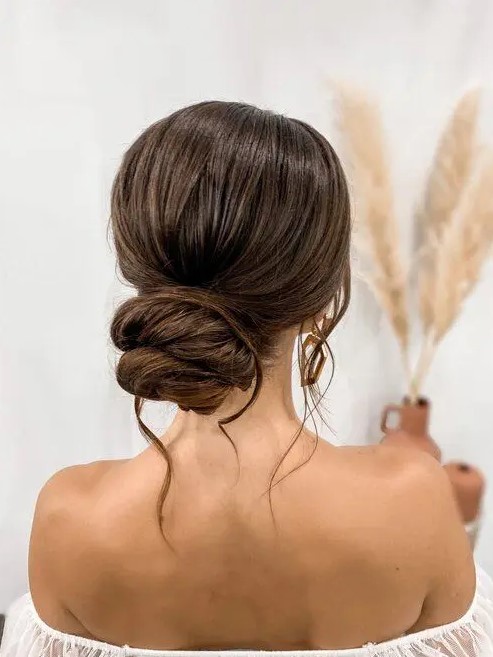 a chic twisted low bun with a bump on top and some waves down is a lovely wedding hairstyle for long and thick hair