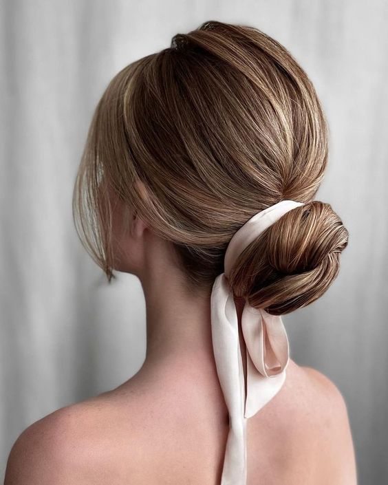 a classy wrapped low bun with a bump on top, a silk ribbon and face framing locks is a chic and stylish idea