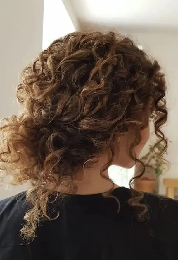 a curly messy low bun with bangs is a timeless idea for girls with curls   looks very pretty and relaxed