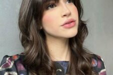 a dark brunette long butterfly haircut with wispy to bottleneck bangs and waves is a cool and girlish idea to try
