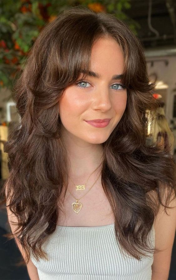 a dreamy brunette butterfly haircut with curtain bangs and waves is a catchy and stylish idea to try on long hair