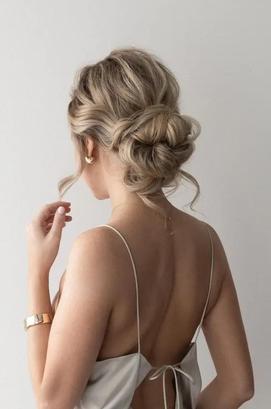 A gorgeous messy woven low bun with a wavy top, some hair down and face frmaing locks is a chic solution for a bridesmaid