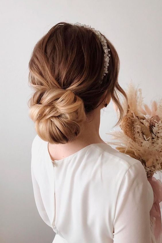 a large twisted low bun with a messy top and a bead and pearl headpiece is a gorgeous idea for a refined bride