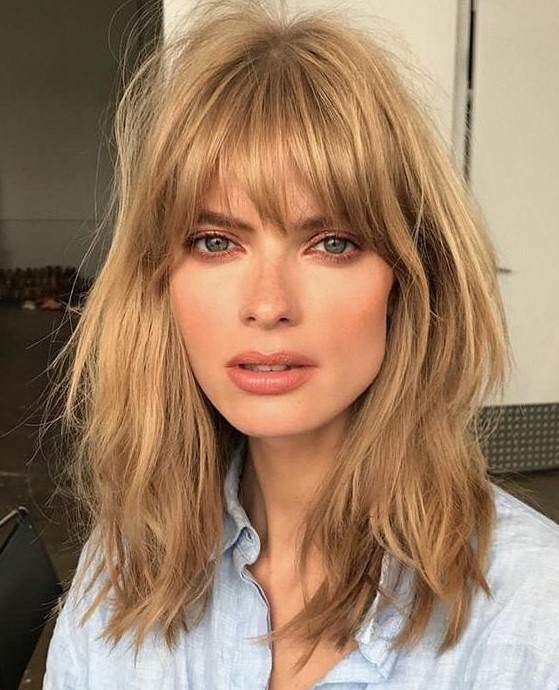a layered honey bronde long bob with shaggy locks and with overgrown and very natural bangs is inspired by the 70s