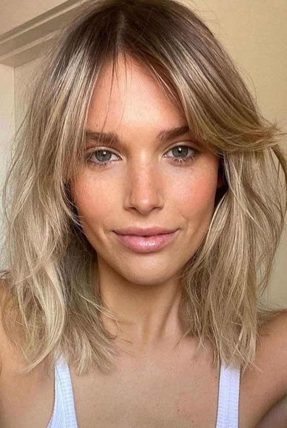 a long and messy blonde bob with a darker root and side bangs, with a lot of dimensional texture is a super chic idea