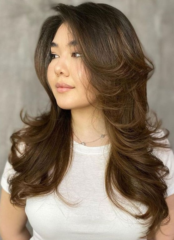 a long dark brunette butterfly haircut with caramel balayage and curled ends plus long curtain bangs